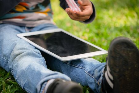 Little school boy kid using tablet computer while sitting in the park. Education technology concept.の写真素材