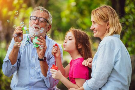 Happy family blows soap bubbles together while going vacation on weekend in the garden park in summer. Kid education and family activities concept.の写真素材