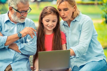 Happy family using laptop computer together in the garden park in summer. Kid education and family activities concept.の写真素材