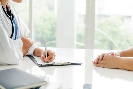 Woman doctor talks to female patient while writing on the patient health record in hospital office. Healthcare and medical service.の写真素材