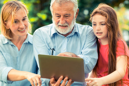 Happy family using laptop computer together in the garden park in summer. Kid education and family...