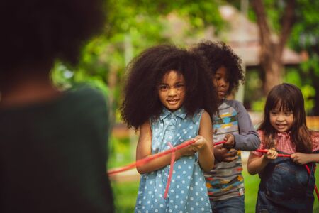 Happy children playing tug of war and having fun during summer camping in the park. Children recreation concept.の写真素材