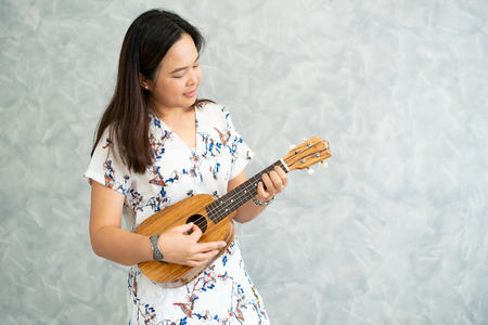 Happy woman musician playing ukulele and singing a song in sound studio. Music lifestyle concept.の写真素材
