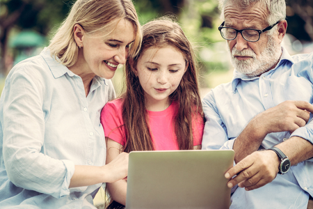 Happy family using laptop computer together in the garden park in summer. Kid education and family activities concept.の写真素材