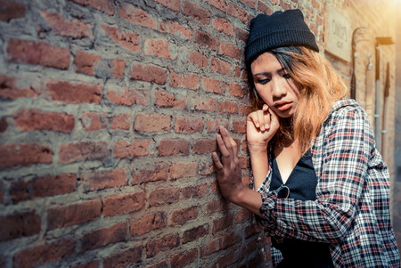 Depressed teenage woman feeling sad alone against brick wall in old town.の写真素材