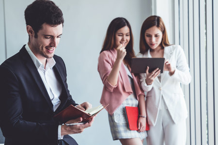 Happy young handsome businessman reading book and working in office with colleagues and friend at workplace.の写真素材