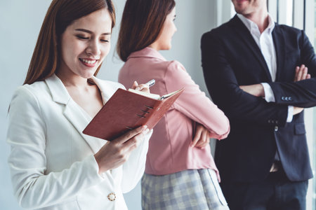 Happy young beautiful businesswoman reading book and working in office with colleagues and friend at workplace.の写真素材