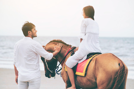 Young couple goes honeymoon horse riding on the beach in summer vacation.の写真素材