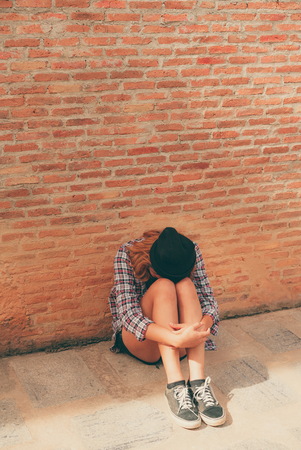 Depressed teenage woman feeling sad alone against brick wall in old town. Education and family failure concept.の写真素材