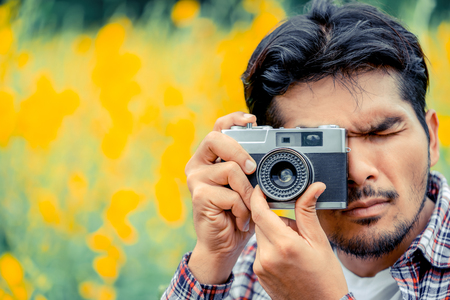 Young hipster man taking photo with old style camera with nature landscape background. Retro and vintage photography concept.の写真素材