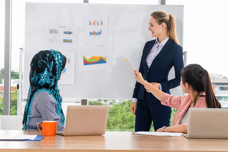 Multicultural working group. Team of businesswomen of different ethnicity, Caucasian, Asian and Arabic working together in team meeting with laptop computer at office. Multiethnic teamwork concept.の写真素材