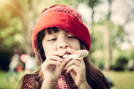 Happy little school girl playing party blow horn on her birthday in the garden in summer. Childhood lifestyles concept.の写真素材