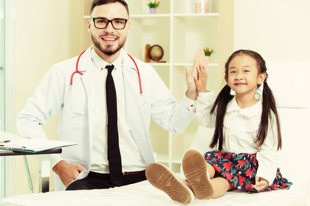 Young male doctor examining little kid in hospital office. The kid is happy and not afraid of the doctor. Medical children healthcare concept.の写真素材