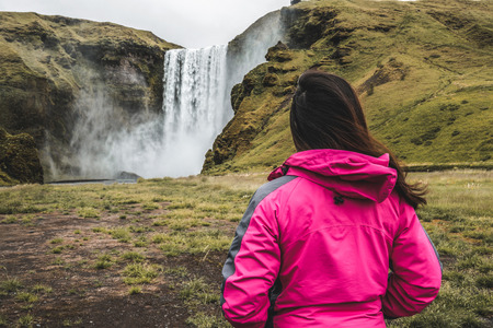 Woman traveler at beautiful scenery of the majestic Skogafoss Waterfall in countryside of Iceland in summer. Skogafoss is the top famous natural landmark and tourist attraction of Iceland and Europe.の写真素材
