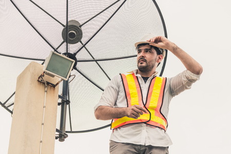 Professional technician or engineer standing on roof top of building working with satellite dish. Concept of repair installation service and telecommunication.の写真素材