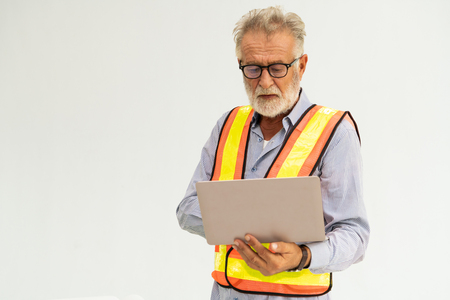 Experienced senior foreman or engineer using laptop computer standing against whiteの写真素材