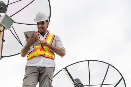 Professional technician or engineer standing on roof top of building working with satellite dish.