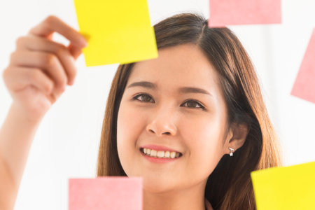 Happy businesswoman thinking creative ideas with sticky notes on glass wall at the office. Work...
