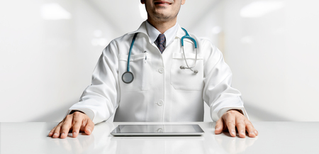 Male doctor sitting at table with tablet computer in hospital office. Medical healthcare staff and doctor service.の写真素材