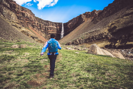 Man traveler hiking in Icelandic summer landscape at the Hengifoss waterfall in Iceland. The waterfall is situated in the eastern part of Iceland.の写真素材