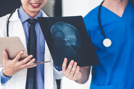Male doctor looking at x ray film of patient head injury while working with another doctor at the hospital. Medical healthcare staff and doctor service.の写真素材