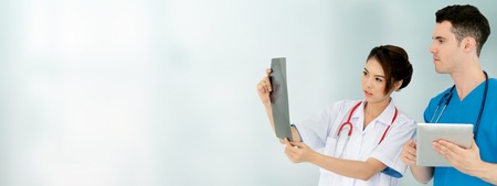Female doctor looking at x ray film while discussing with another doctor holding a tablet computer at the hospital. Medical healthcare staff and doctor service.の写真素材