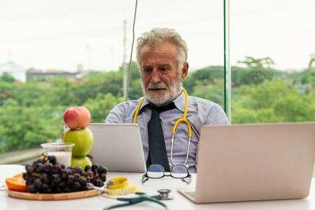 Senior male nutritionist doctor working with laptop computer on table in the hospital office. Dieting and healthy eating concept.の写真素材
