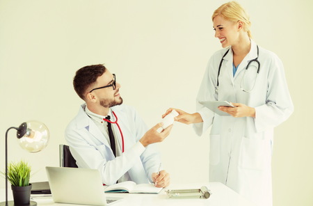 Doctor at hospital office passing medicine bottle to another doctor while having discussion about patients referral.の写真素材