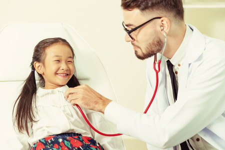 Young male doctor examining little kid in hospital office. The kid is happy and not afraid of the doctor. Medical children healthcare concept.の写真素材