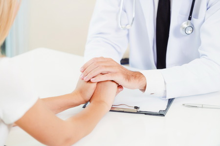 Male doctor soothes a female patient in hospital office while holding the patients hands. Healthcare and medical service.の写真素材