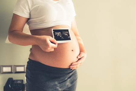 Pregnant woman feeling happy at home while taking care of her child. The young expecting mother holding baby in pregnant belly. Maternity prenatal care and woman pregnancy concept.の写真素材