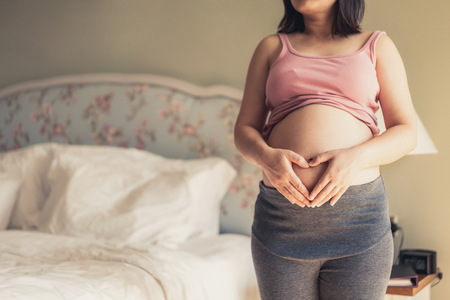 Pregnant woman feeling happy at home while taking care of her child. The young expecting mother holding baby in pregnant belly. Maternity prenatal care and woman pregnancy concept.の写真素材