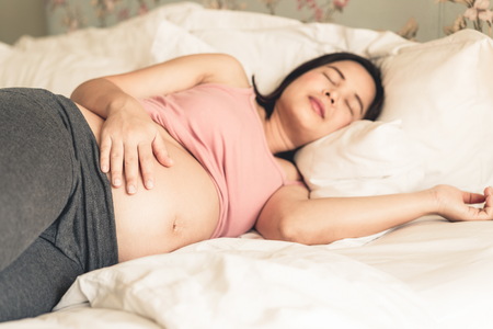 Pregnant woman feeling happy at home while taking care of her child. The young expecting mother holding baby in pregnant belly. Maternity prenatal care and woman pregnancy concept.の写真素材