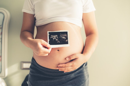 Pregnant woman feeling happy at home while taking care of her child. The young expecting mother holding baby in pregnant belly. Maternity prenatal care and woman pregnancy concept.の写真素材
