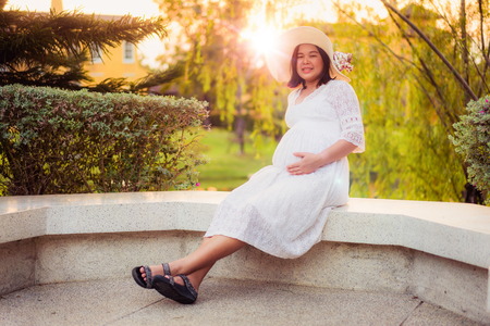 Pregnant woman feeling happy with new life at garden home while take care of her child. The young expecting mother holding baby in pregnant belly. Maternity prenatal care and woman pregnancy concept.の写真素材