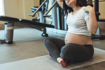 Active pregnant woman exercise in fitness center at yoga room. The young expecting mother holding baby in pregnant belly. Maternity prenatal care and woman pregnancy concept.の写真素材