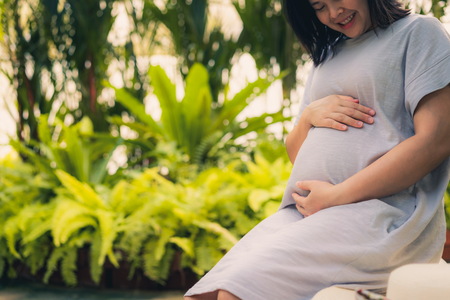 Pregnant woman feeling happy at home while taking care of her child. The young expecting mother holding baby in pregnant belly. Maternity prenatal care and woman pregnancy concept.の写真素材