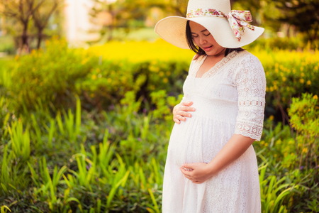 Pregnant woman feeling happy with new life at garden home while take care of her child. The young expecting mother holding baby in pregnant belly. Maternity prenatal care and woman pregnancy concept.の写真素材
