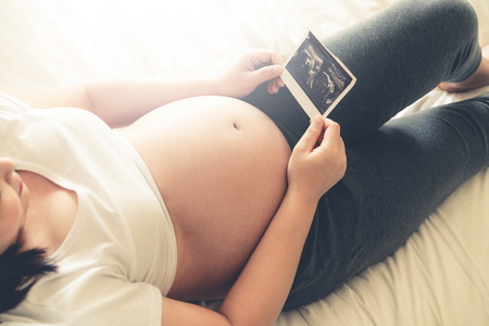 Pregnant woman feeling happy at home while taking care of her child. The young expecting mother holding baby in pregnant belly. Maternity prenatal care and woman pregnancy concept.の写真素材