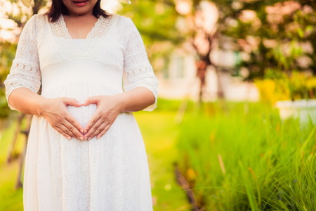 Pregnant woman feeling happy with new life at garden home while take care of her child. The young expecting mother holding baby in pregnant belly. Maternity prenatal care and woman pregnancy concept.の写真素材