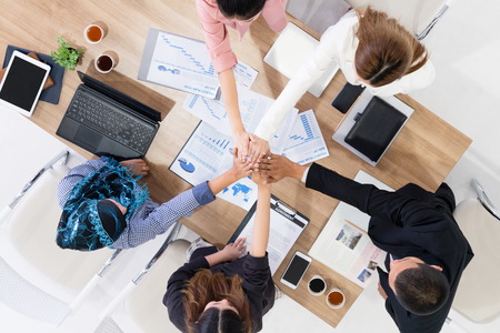 Businessmen and businesswomen joining hands in group meeting at multicultural office room showing teamwork, support and unity in business. Diversity workplace and corporate people working concept.の写真素材