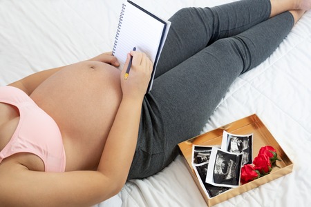Pregnant woman feeling happy at home while taking care of her child. The young expecting mother holding baby in pregnant belly. Maternity prenatal care and woman pregnancy concept.の写真素材