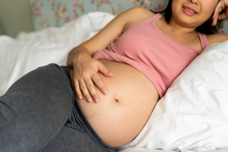 Pregnant woman feeling happy at home while taking care of her child. The young expecting mother holding baby in pregnant belly. Maternity prenatal care and woman pregnancy concept.の写真素材