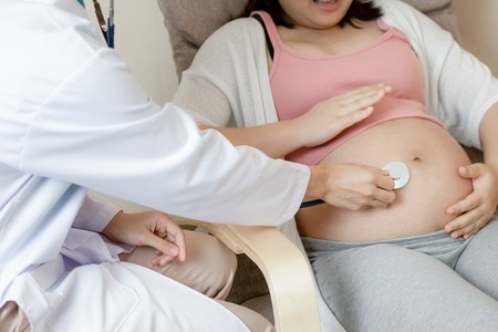 Happy pregnant woman visit gynecologist doctor at hospital or medical clinic for pregnancy consultant. Doctor examine pregnant belly for baby and mother healthcare check up. Gynecology concept.の写真素材