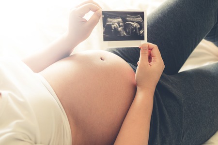 Pregnant woman feeling happy at home while taking care of her child. The young expecting mother holding baby in pregnant belly. Maternity prenatal care and woman pregnancy concept.の写真素材