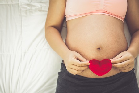 Pregnant woman feeling happy at home while taking care of her child. The young expecting mother holding baby in pregnant belly. Maternity prenatal care and woman pregnancy concept.の写真素材
