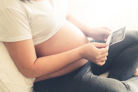 Pregnant woman feeling happy at home while taking care of her child. The young expecting mother holding baby in pregnant belly. Maternity prenatal care and woman pregnancy concept.の写真素材