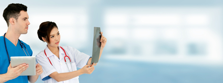 Female doctor looking at x ray film while discussing with another doctor holding a tablet computer at the hospital. Medical healthcare staff and doctor service.の写真素材