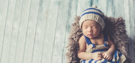 Adorable newborn baby sleeping in cozy room. Cute happy infant baby portrait with sleepy face in bed. Soft focus at the baby eyes. Newborn nursery care and baby lullaby concept.の写真素材