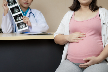 Happy pregnant woman visit gynecologist doctor at hospital or medical clinic for pregnancy consultant. Doctor examine pregnant belly for baby and mother healthcare check up. Gynecology concept.の写真素材